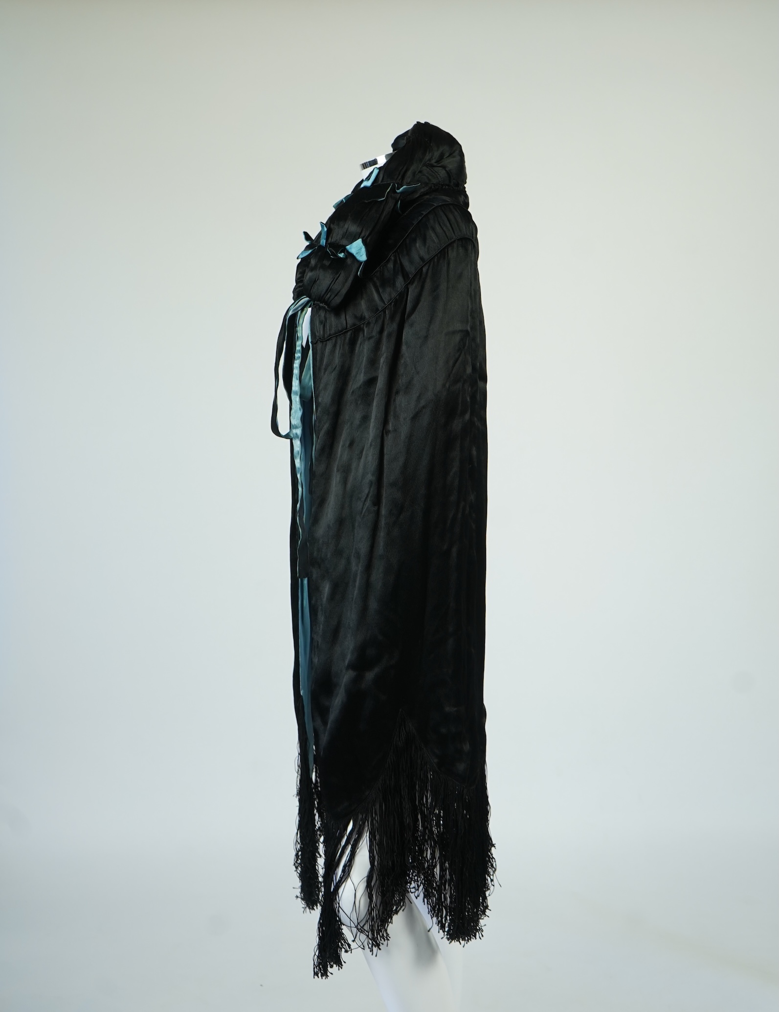 A 1920's ladies blue lined, black silk opera cape. Designed with a rushed ornate collar and scalloped and fringed lower edge. 95cm long fron neck to base. Condition - stained near the front edge, possibly removable with